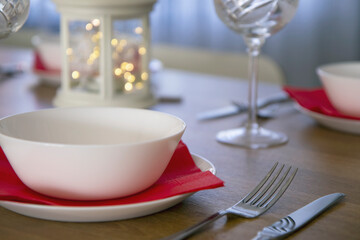 Beautiful table setting for Christmas dinner with clear glasses, china plates and red napkins.