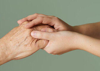 Close-up of the hand of a young woman holding the hand of an elderly lady on a light green background