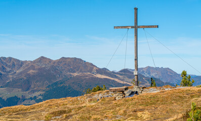 Fototapeta na wymiar Wooden cross on the top of Gerlosstein in Austrian Alps with mountain panorama in the back on a sunny day of autumn with blue sky above. Mountain top on a sunny day.