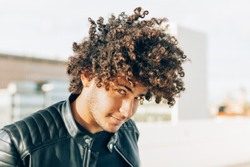 outdoors portrait of young man with a lively and sympathetic look with curly hair looking in camera