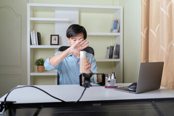 Young adult Asian beauty video blogger man filming, online live streaming his video blog about male cosmetic, male skincare. Guy looking camera to show new skin care for men product, teaching make up.