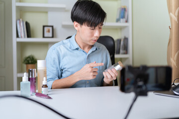 Young adult Asian beauty video blogger man filming, online live streaming his video blog about male cosmetic, male skincare. Guy looking camera to show new skin care for men product, teaching make up.
