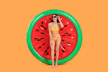 Happy young woman with beautiful suntan, sunglasses and inflatable mattress against orange background