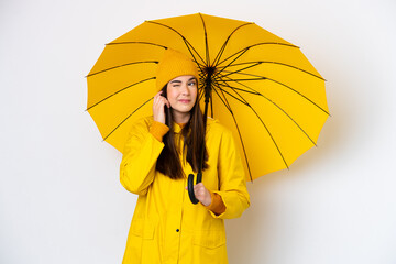 Young Brazilian woman with rainproof coat and umbrella isolated on white background frustrated and covering ears