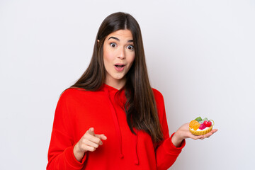 Young Brazilian woman holding a tartlet isolated on white background surprised and pointing front