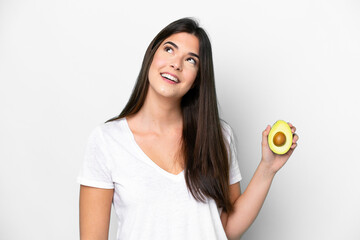 Young Brazilian woman holding an avocado isolated on white background looking up while smiling