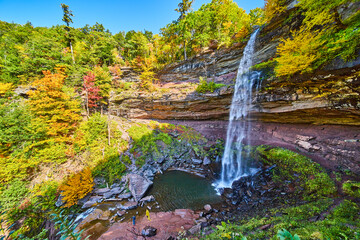 Waterfall pours over layered cliffs surrounded by fall forests from side middle