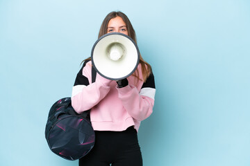 Young sport woman with sport bag isolated on blue background shouting through a megaphone