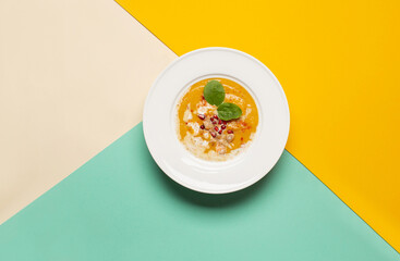 top view of pumpkin puree soup in white plate on beige yellow green background with free space for text
