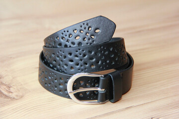Black leather women's trouser belt with a decorative pattern on a brown wooden background.