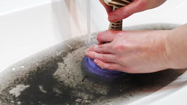 women's hands with plunger and dirty sink with the clog in the pipe.