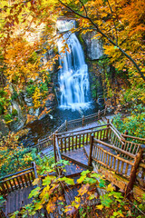 Obraz premium Boardwalk stairs lead down to stunning large waterfall over cliffs surrounded by yellow fall foliage