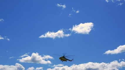 Camera movement from right to left as helicopter flies through blue cloudy sky and descends in preparation for landing. Airplane wing against sky with cumulus clouds. Helicopter is preparing to land.