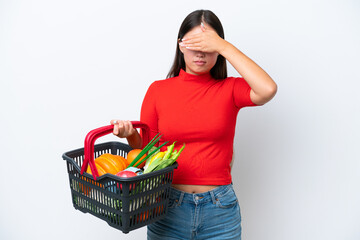 Obraz na płótnie Canvas Young Asian woman holding a shopping basket full of food isolated on white background covering eyes by hands. Do not want to see something
