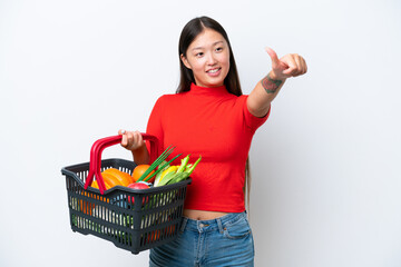 Fototapeta na wymiar Young Asian woman holding a shopping basket full of food isolated on white background giving a thumbs up gesture