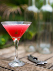 red cocktail with ice in glass with stem on wooden surface