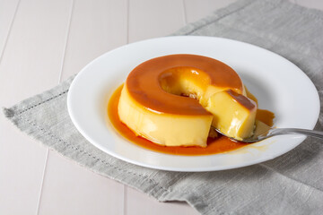 pudim de leite, also known as flan or milk pudding, isolated on white table with grey cloth. bitten...