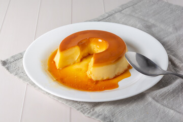 pudim de leite, also known as flan or milk pudding, isolated on white table with grey cloth. bitten slice with a metallic spoon concept of traditional brazilian dessert