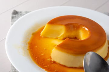 pudim de leite, also known as flan or milk pudding, isolated on white table with grey cloth. bitten slice with a metallic spoon concept of traditional brazilian dessert