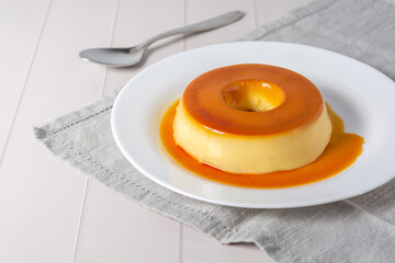 pudim de leite, also known as flan or milk pudding, isolated on white table with grey cloth. bitten slice with a metallic spoon concept of traditional brazilian dessert