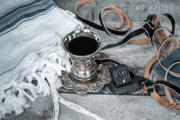 On the table is a silver glass for kiddush with shabbat wine, next to it is a folded tallit and...