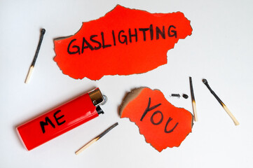 Red card with the word "gaslighting", with a lighter next to it with the word "me", and burnt red card with the word "you". Dynamics of gaslighting.
