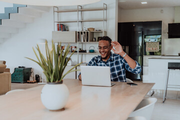 African American man in glasses sitting at a table in a modern living room, using a laptop for business video chat, conversation with friends and entertainment