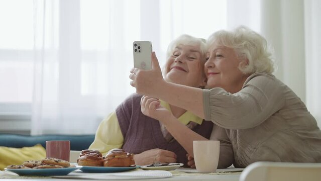 Cheerful senior sisters taking a selfie on phone while meeting for tea, friends
