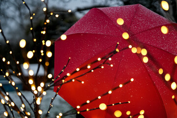 Aufgespannter Schirm im Schneefall vor weihnachtlicher Beleuchtung