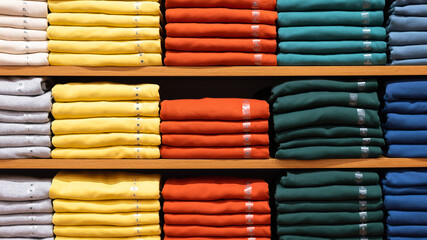 Stacked of multi-color cotton shirts which are folded on the shelf at the clothing store. Object...
