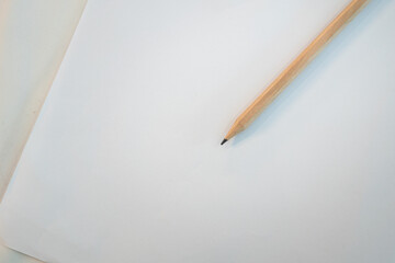 A wooden sharped pencil is placed on white empty paper sheet. Close-up and selective focus at the pencil part.