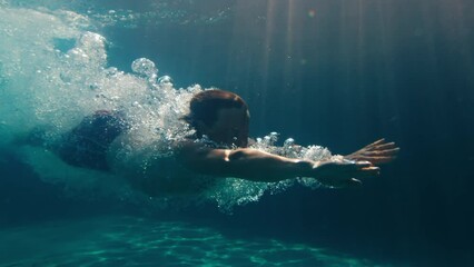 Man dives in the pool. Underwater view of the person diving in the pool and gliding underwater with bubbles - Powered by Adobe