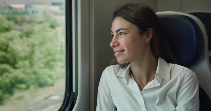 Cinematic shot of Young Woman Looking Through Window While Traveling by Train Through Green Landscape. Happy Female Smiling and Feeling Excited about New Opportunities After Arriving to the Suburbs