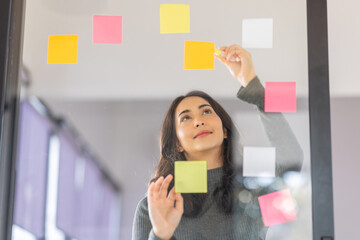 Business female employee with many conflicting priorities arranging sticky notes commenting and brainstorming on work priorities colleague in a modern office.