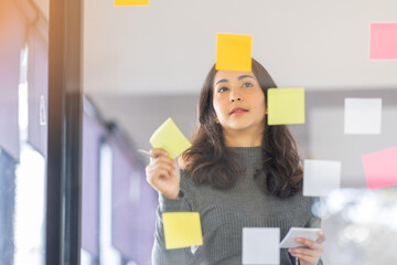 Business female employee with many conflicting priorities arranging sticky notes commenting and brainstorming on work priorities colleague in a modern office.