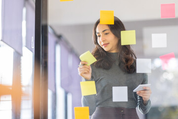 Business female employee with many conflicting priorities arranging sticky notes commenting and brainstorming on work priorities colleague in a modern office. - obrazy, fototapety, plakaty