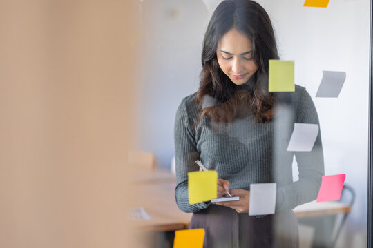 Business female employee with many conflicting priorities arranging sticky notes commenting and brainstorming on work priorities colleague in a modern office.