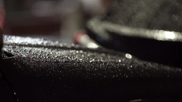 Black car surface and rain drops on it. A car hood at night with tiny rain drops on it which sparkle reflecting street lamps. Rainy night in the city. 