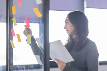 Business female employee with many conflicting priorities arranging sticky notes commenting and...
