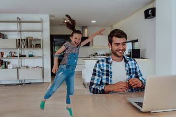 Obraz premium Work from home. Daughter interrupting her father while he is having a business online conversation on his laptop while sitting in modern living room