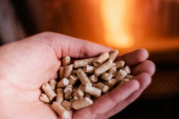 Hand holding pellets in front of the glass of a stove with a beautiful flame