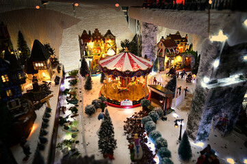 Christmas village with a carousel with little horses, ice skaters, a goose pond and snow-covered trees