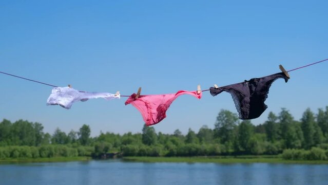 set of bright women panties is drying on a rope by the river, swaying in the wind. women underwear is hanging on a rope with clothespins. slow motion. selective focus.