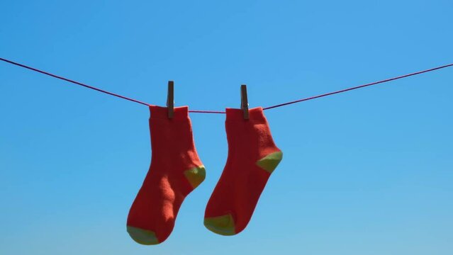 pair of orange socks closeup drying after washing on rope, swaying in the wind. socks hang on rope with clothespins against the blue sky. selective focus.
