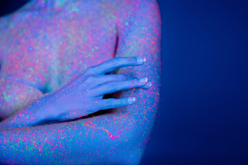 partial view of woman with bright neon stains on body isolated on dark blue.