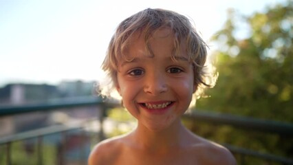 Portrait of a handsome small boy close up face looking at camera standing outdoors during beautiful summer day