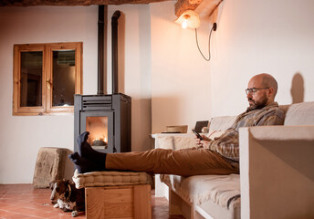 man in his forties looking at mobile phone, pellet cooker, dog resting on couch, petting dog. Rustic design dining room