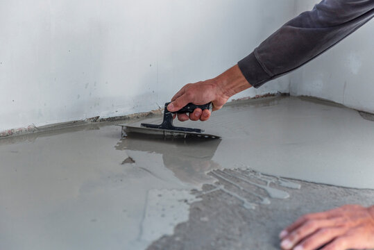 Grey self-leveling screed, new floor layer, man hand.