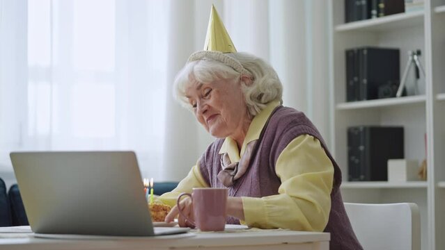 Joyful Grandma Blowing Out Candles On Cake During Video Call, Lockdown Birthday