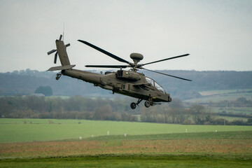 Fototapeta na wymiar British army AH-64E Boeing Apache Attack helicopter (ZM722 ArmyAir606) moves forward from hover in to flight over a grass meadow, Wiltshire UK 